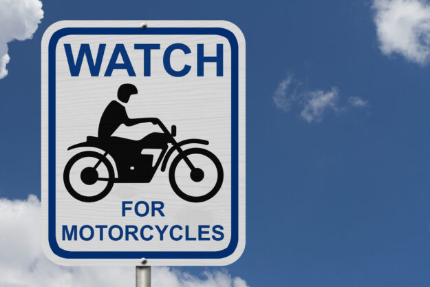 Motorcyclist Fatally Injured In Hit-and-Run Accident - Watch For Motorcycles Warning Sign, An road warning sign with words Watch For Motorcycles and a motorcycle icon with blue sky background